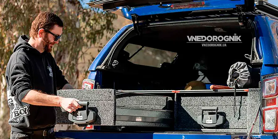 Счастливый мужчина с легкостью открывает полностью загруженный выдвижной ящик в своем внедорожнике, демонстрируя удобство и радость от организованного пространства в путешествии.